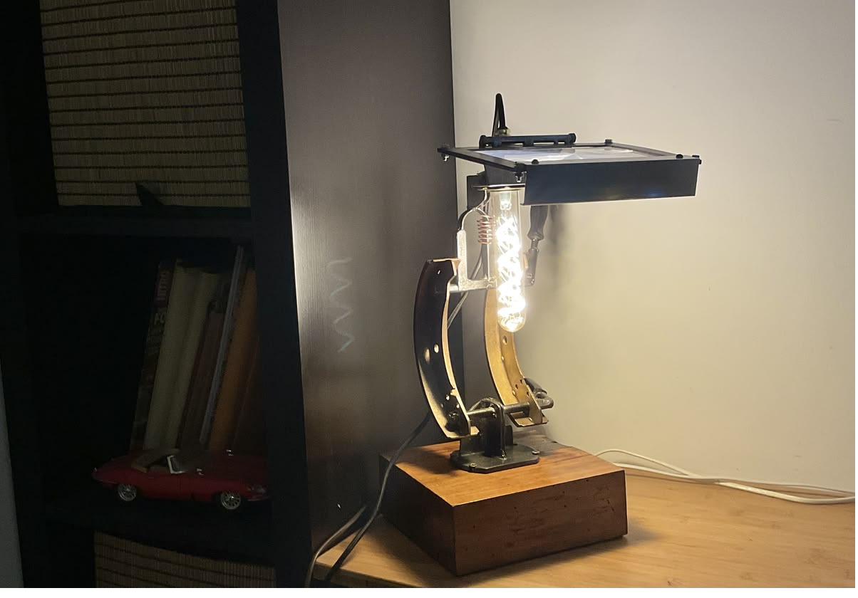 Le Lumicroscope allumé sur un meuble : l'ampoule à filament éclaire à travers l'écran-loupe, ambiance chaleureuse d'atelier